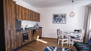 A modern kitchen with wooden cabinets, a dining area with a round table and chairs, and a patterned rug on the floor.