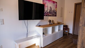 A modern living room with a flat-screen TV mounted on the wall, a wooden bench, a white entertainment unit, and a cityscape painting.