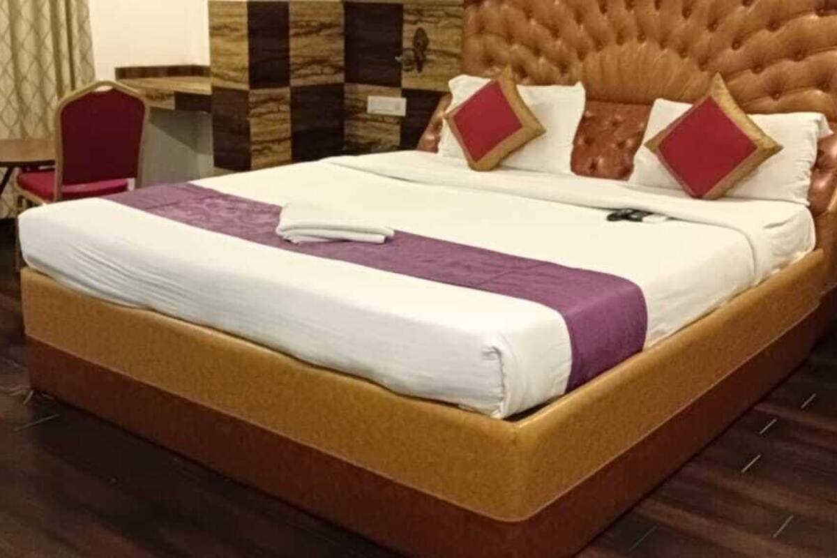 A hotel room with a large bed, two red chairs, a small table, and a wooden headboard.