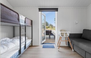 Una habitación pequeña con una cama litera, una mesita con una silla y un sofá.