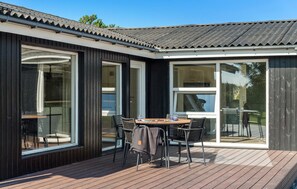 Un área de comedor exterior moderna con cubierta de madera, sillas de metal y una mesa.