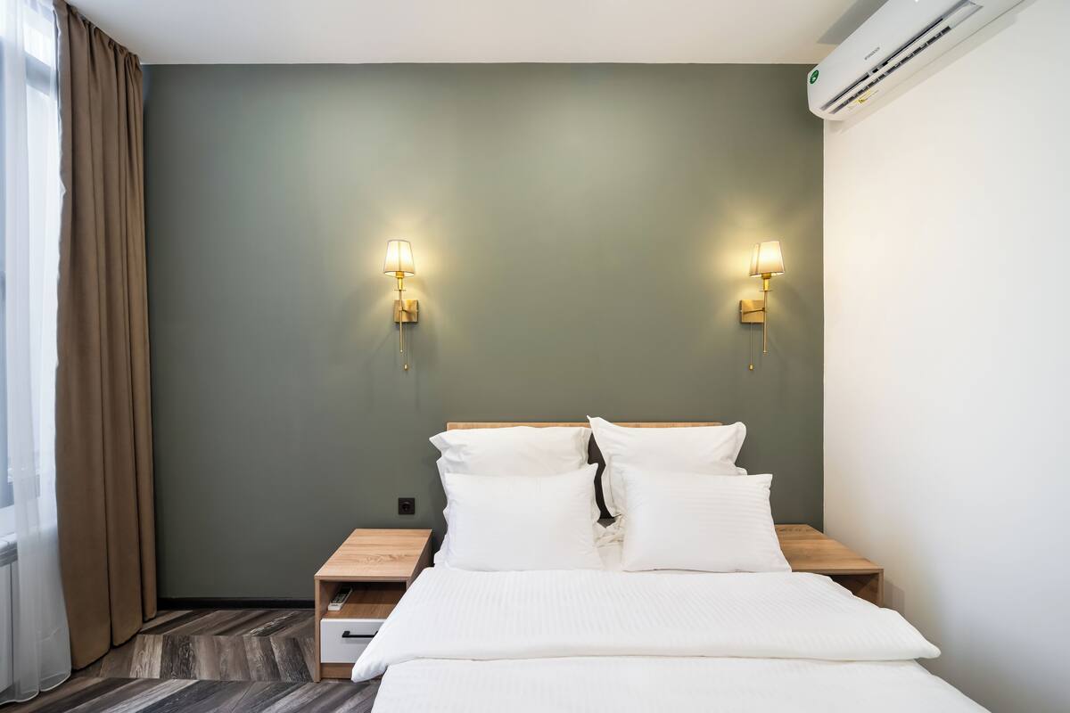 Una habitación de hotel con una cama, dos mesitas de noche y un equipo de aire acondicionado.