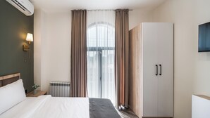 Ein Hotelzimmer mit Bett, Schrank, Heizkörper und einem an der Wand montierten Fernseher.