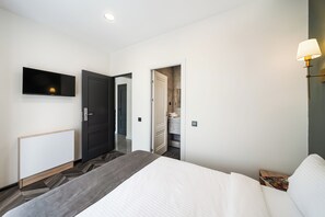 A modern hotel room with a bed, a flat-screen TV, a bedside table with a lamp, and a bathroom visible through an open door. - Estetico Boutique Hotel (Yerevan)