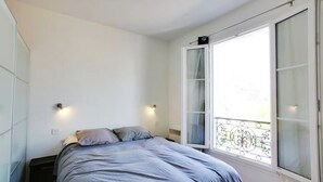 A bedroom with a bed, a window with a balcony, and a wardrobe.