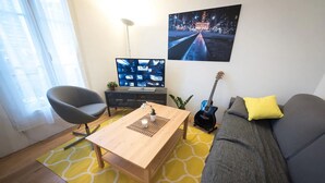 A modern living room with a wooden coffee table, a grey sofa with a yellow pillow, a black guitar, a TV on a black stand, and a yellow patterned rug.