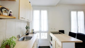 A modern kitchen with white cabinets, a sink, a stove, and a dining area with a black chair.
