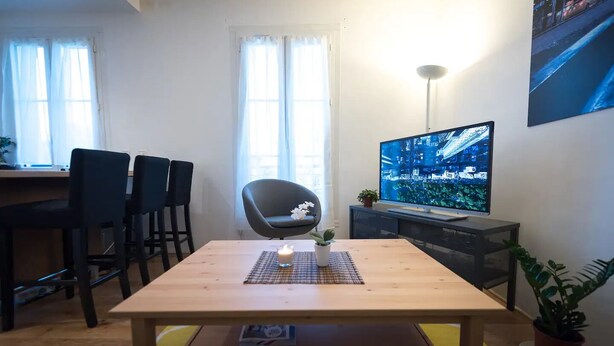 A modern living room with a wooden table, a TV on a stand, and a chair.