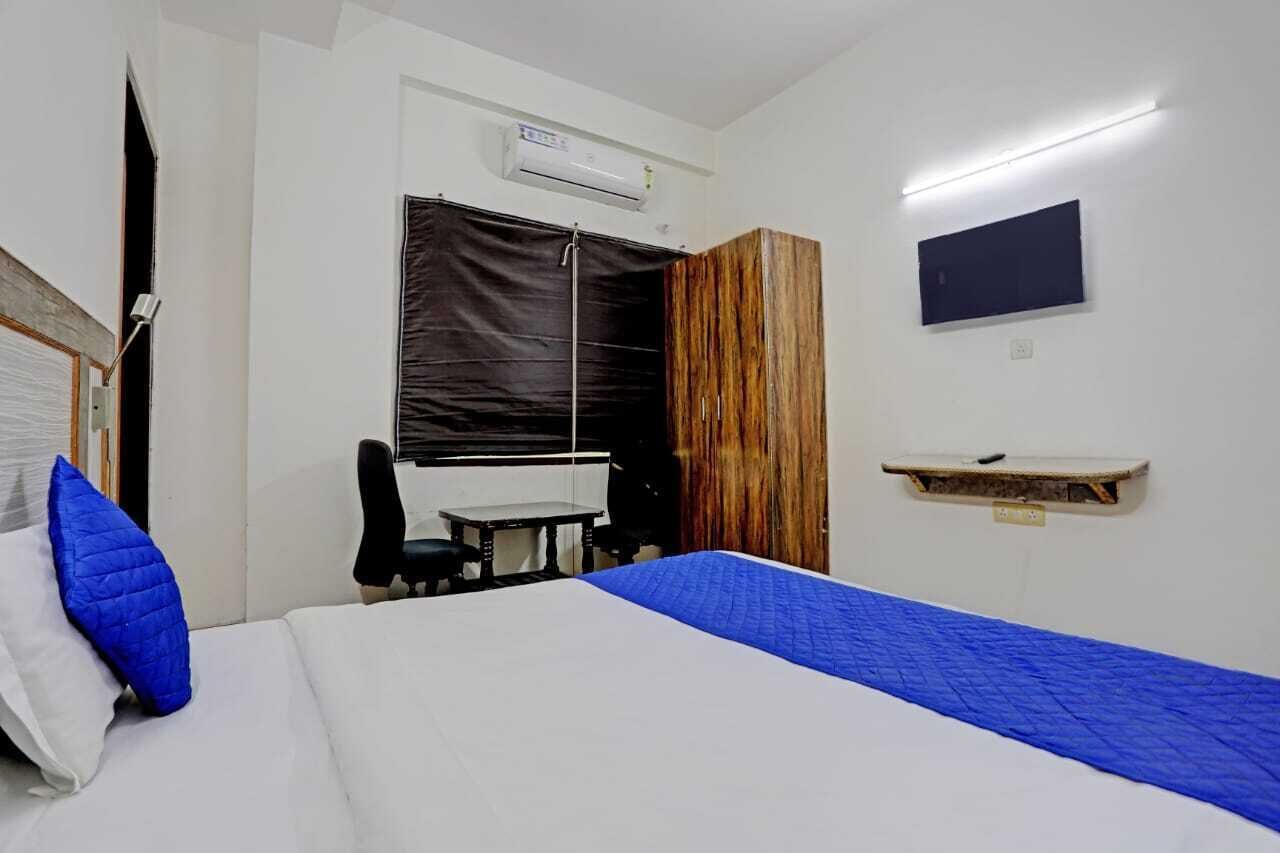 A hotel room with a bed, a desk, a chair, a TV, and an air conditioning unit.