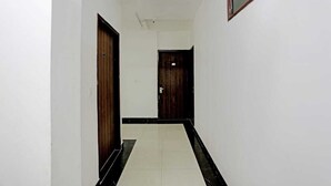 Un pasillo estrecho con paredes blancas y suelo de baldosas negras que conduce a una puerta de madera oscura.