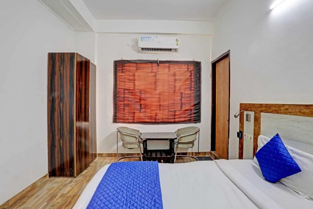 A hotel room with a bed, a desk with two chairs, an air conditioning unit, and a window with a curtain.