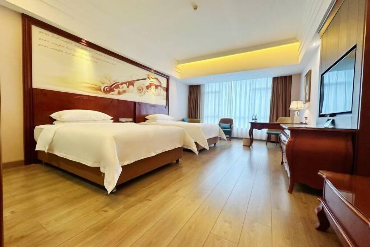A hotel room with a large bed, a desk, a chair, and a television.