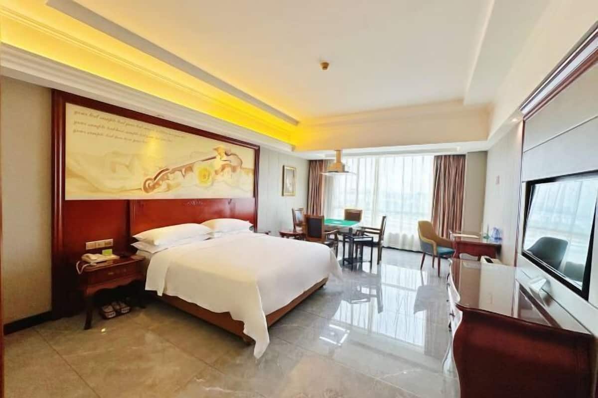 A hotel room with a large bed, a desk, a TV, and a dining area.