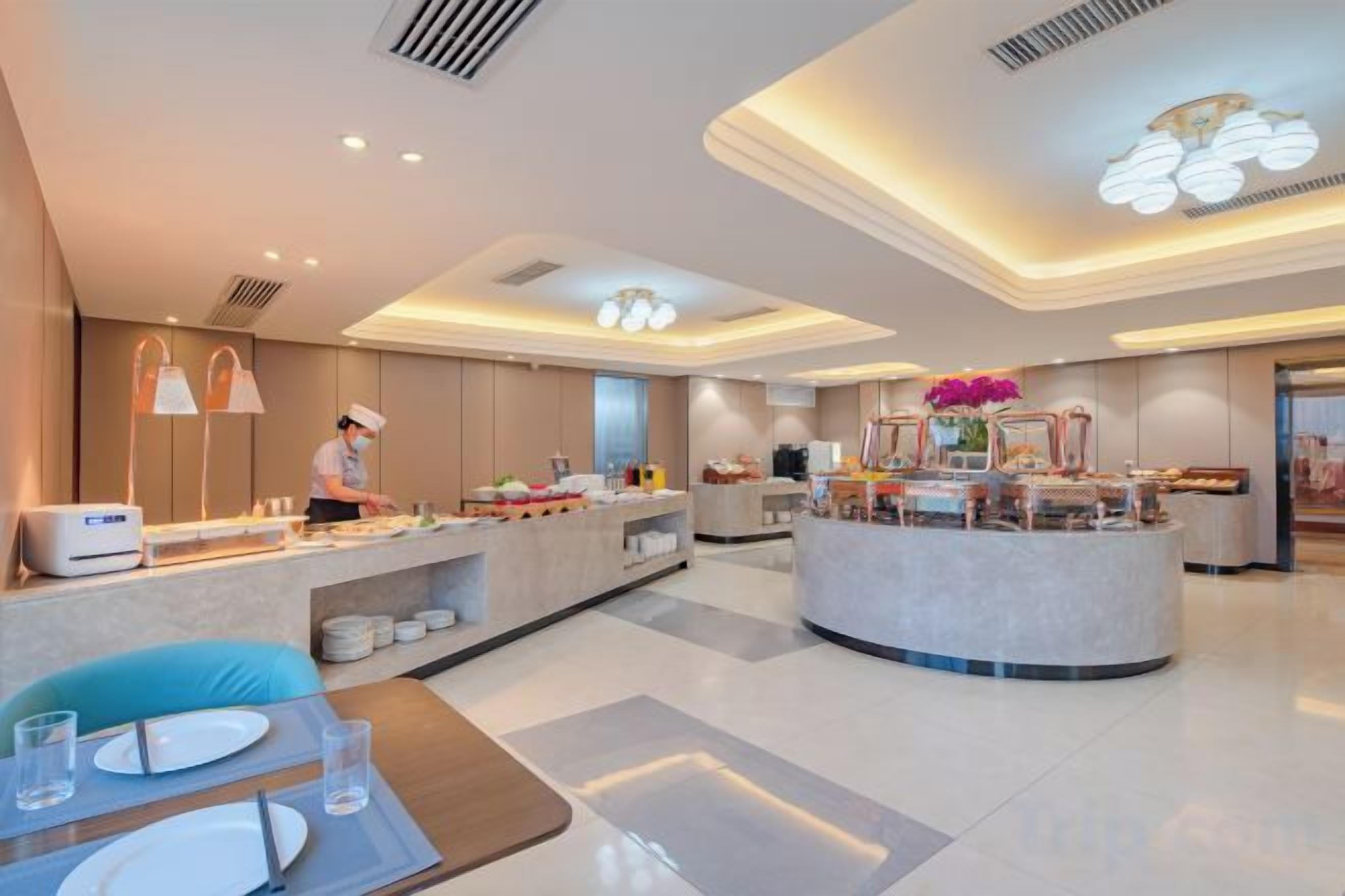 A modern hotel lobby with a central reception desk, seating area, and a buffet.