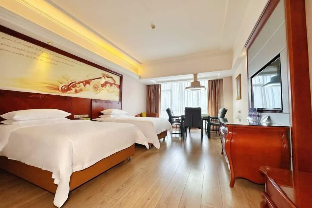 A hotel room with two beds, a desk, a chair, a TV, and a large wall mural.