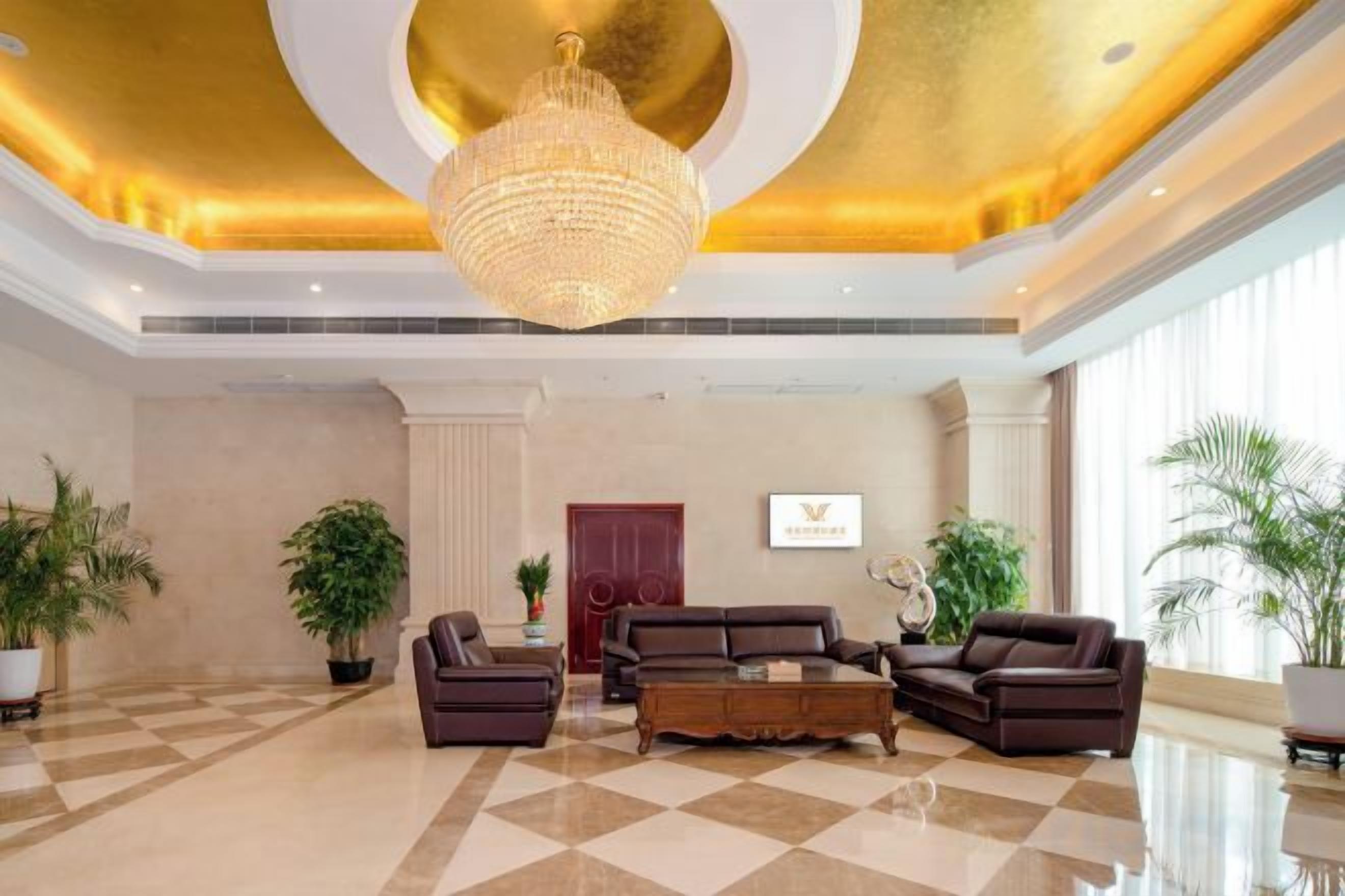 A spacious lobby with a chandelier, sofas, and potted plants.