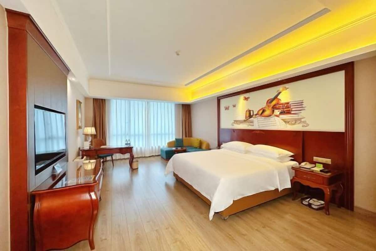 A hotel room with a bed, a desk, a chair, a TV, and a large window with curtains.