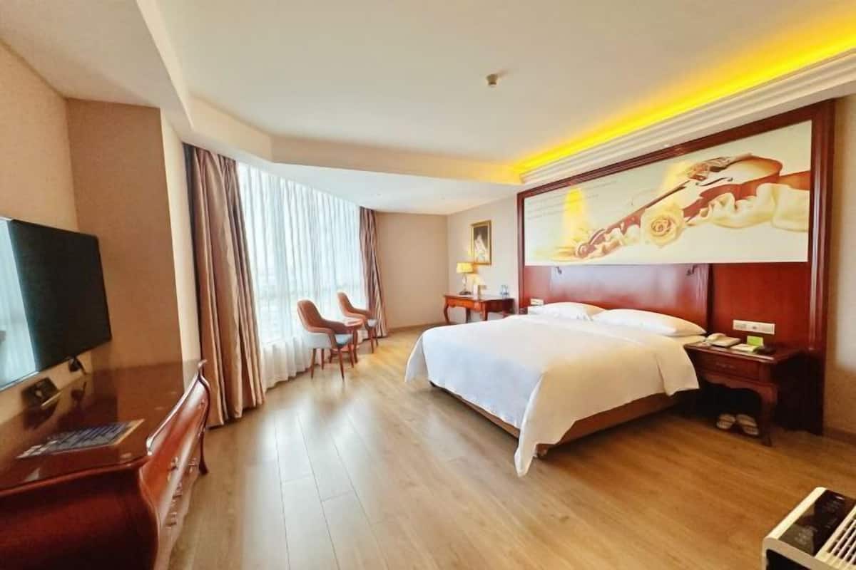 A hotel room with a bed, a desk with a chair, a television, and a painting on the wall.
