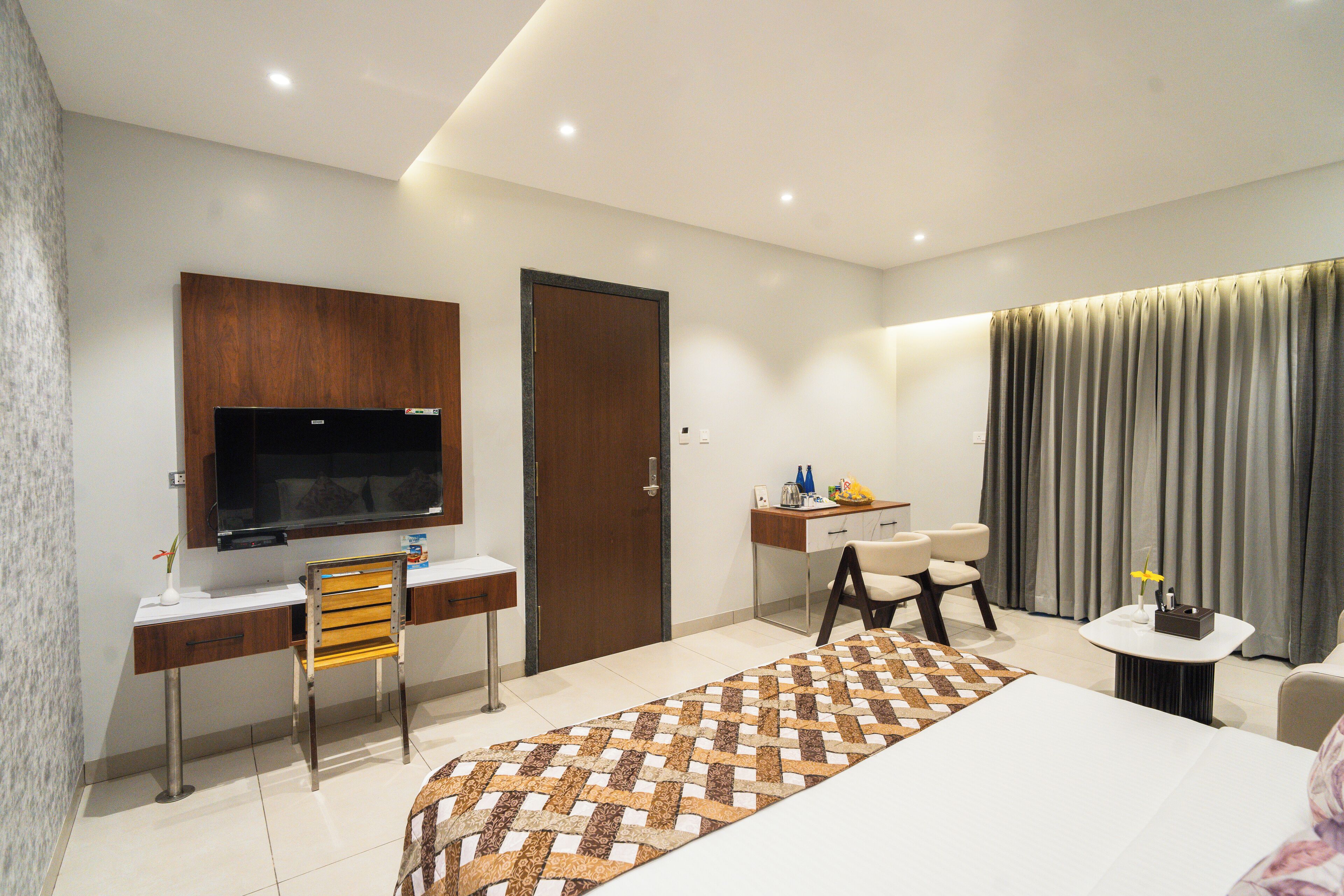 Ein modernes Hotelzimmer mit einem großen Bett, einem Schreibtisch mit Stuhl, einem Fernseher, einer Schreibtischlampe und einem kleinen Tisch mit Lampe.