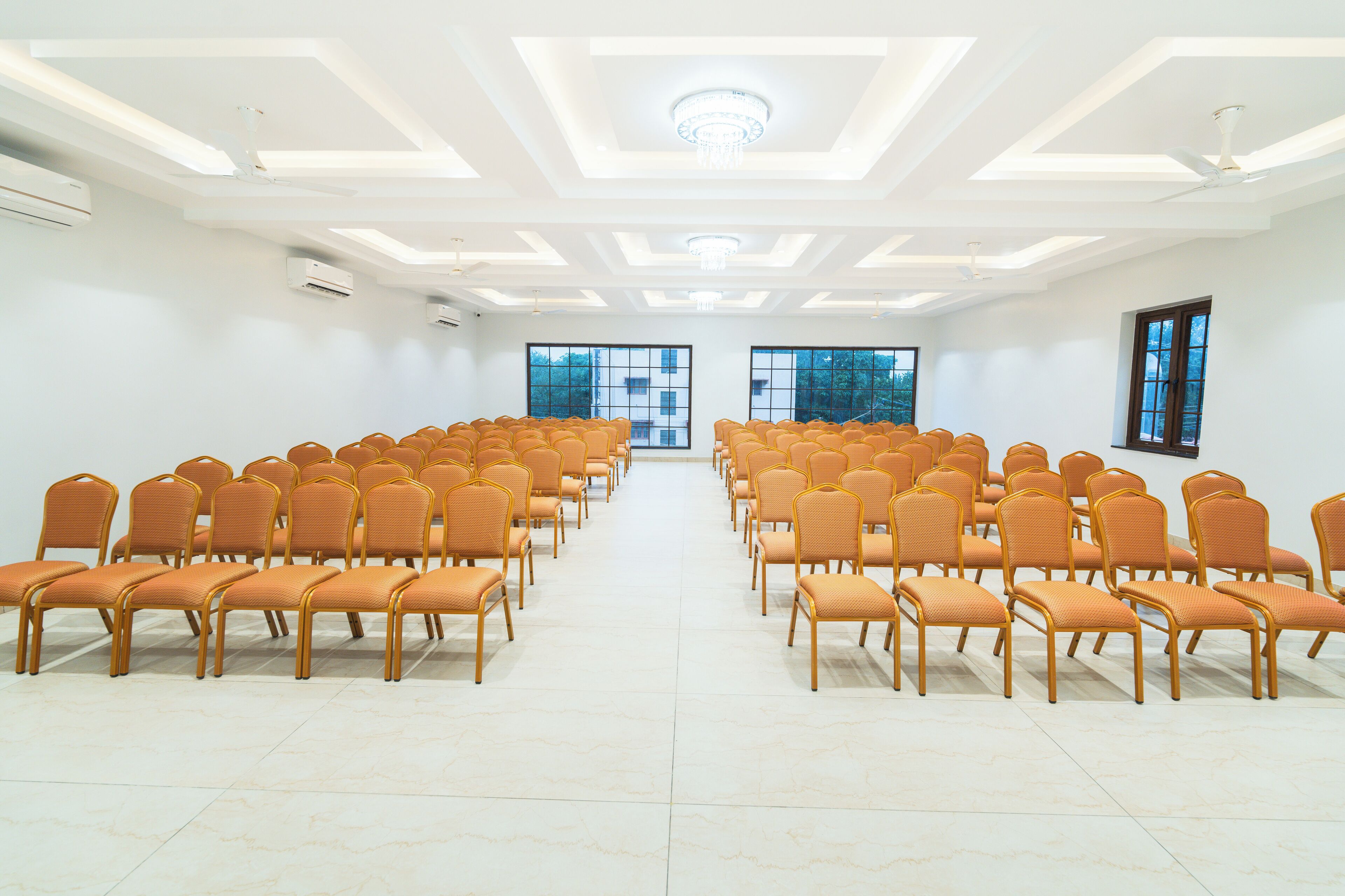 Un salón de conferencias con hileras de sillas anaranjadas, ventanas amplias y un diseño moderno del techo.