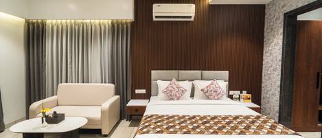 A modern hotel room with a bed, a sofa, a small table, and an air conditioning unit.
