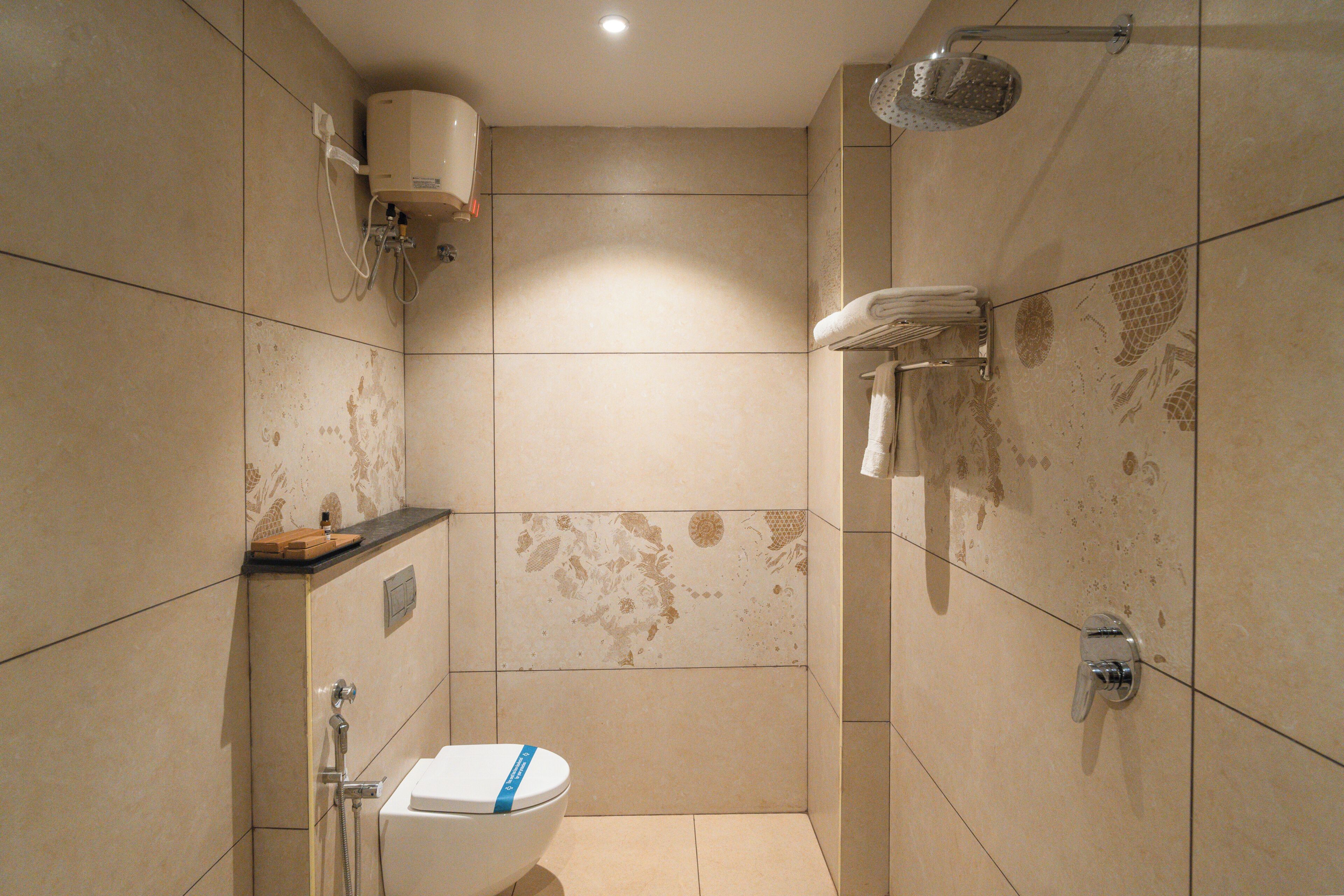 A small, tiled bathroom with a toilet, shower, and towel rack.