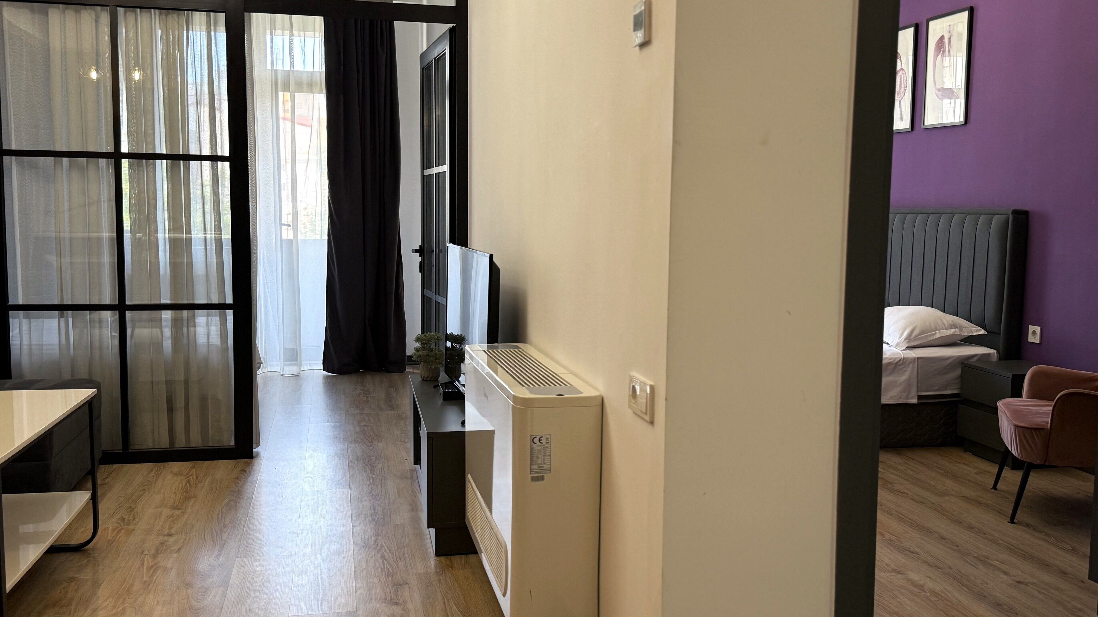 Habitación de hotel con cama, escritorio, silla, radiador y ventana con cortinas.