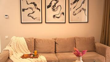 Ein Wohnzimmer mit einem beigen Sofa, einem Glastisch und drei abstrakten Bildern an der Wand.