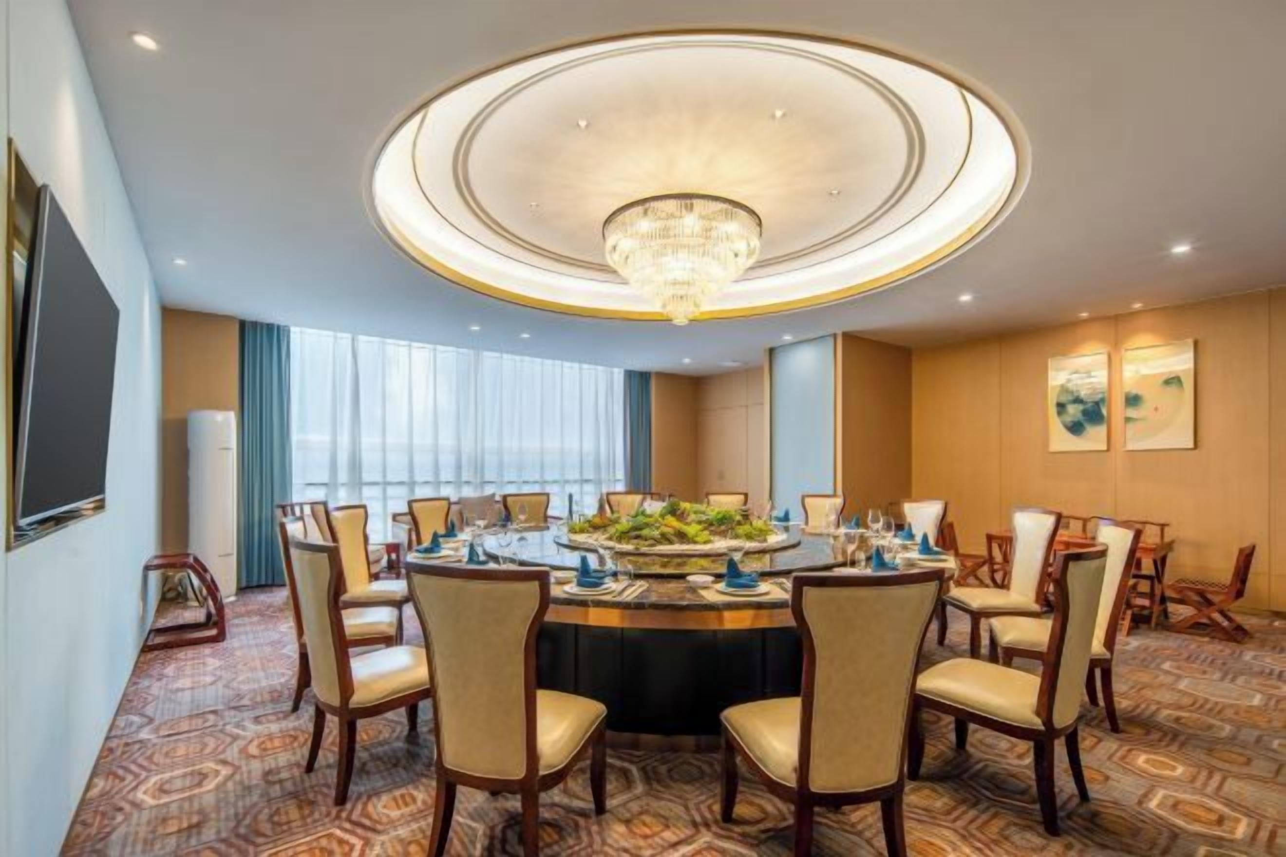 A conference room with a round table, chairs, a chandelier, and a large window.