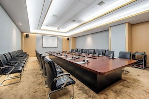 Un salón de conferencias con una mesa larga, varias sillas, una pantalla de proyector y piso alfombrado.