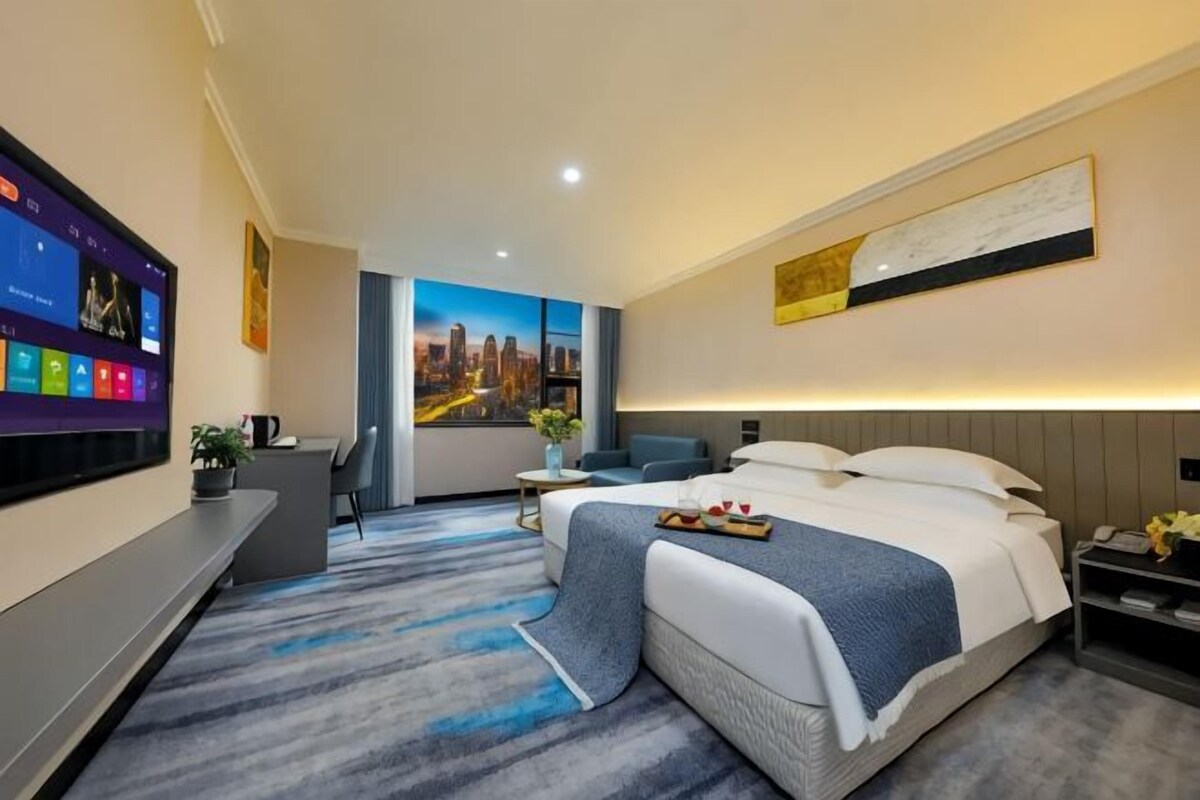A modern hotel room with a large bed, a desk, a flat-screen TV, and a cityscape view.