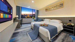 A modern hotel room with a large bed, a desk, and a TV displaying a cityscape view.