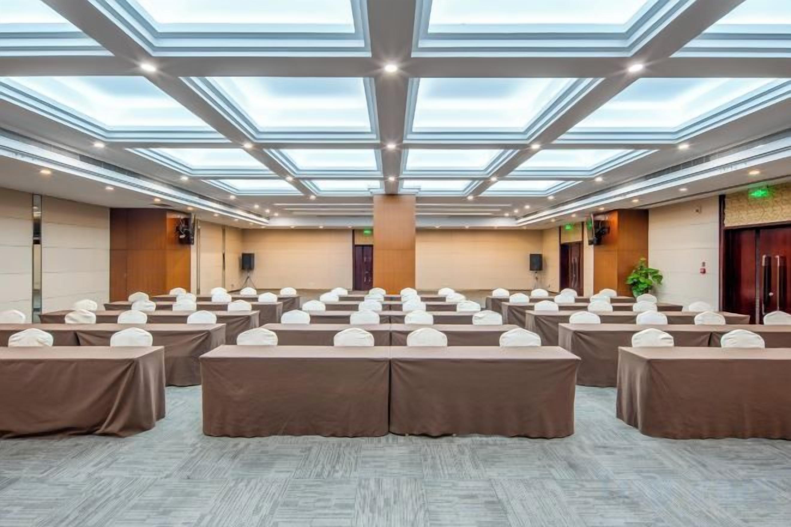 A conference room with a high ceiling, skylights, and rows of tables with white chairs.