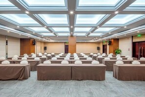 Un salón de conferencias con techo alto, tragaluces y filas de mesas con sillas blancas.