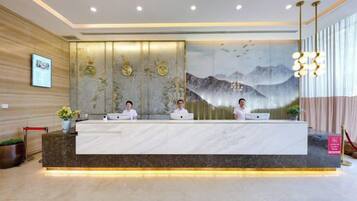 A reception desk with three staff members, a large wall mural, and a modern chandelier.