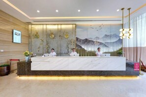 A reception desk with three staff members, a large wall mural, and a modern chandelier. - Wuhan Huazun Tianlun Hotel (Wuhan)
