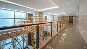 A modern hotel corridor with a glass railing, pendant lighting, and a view of the city.
