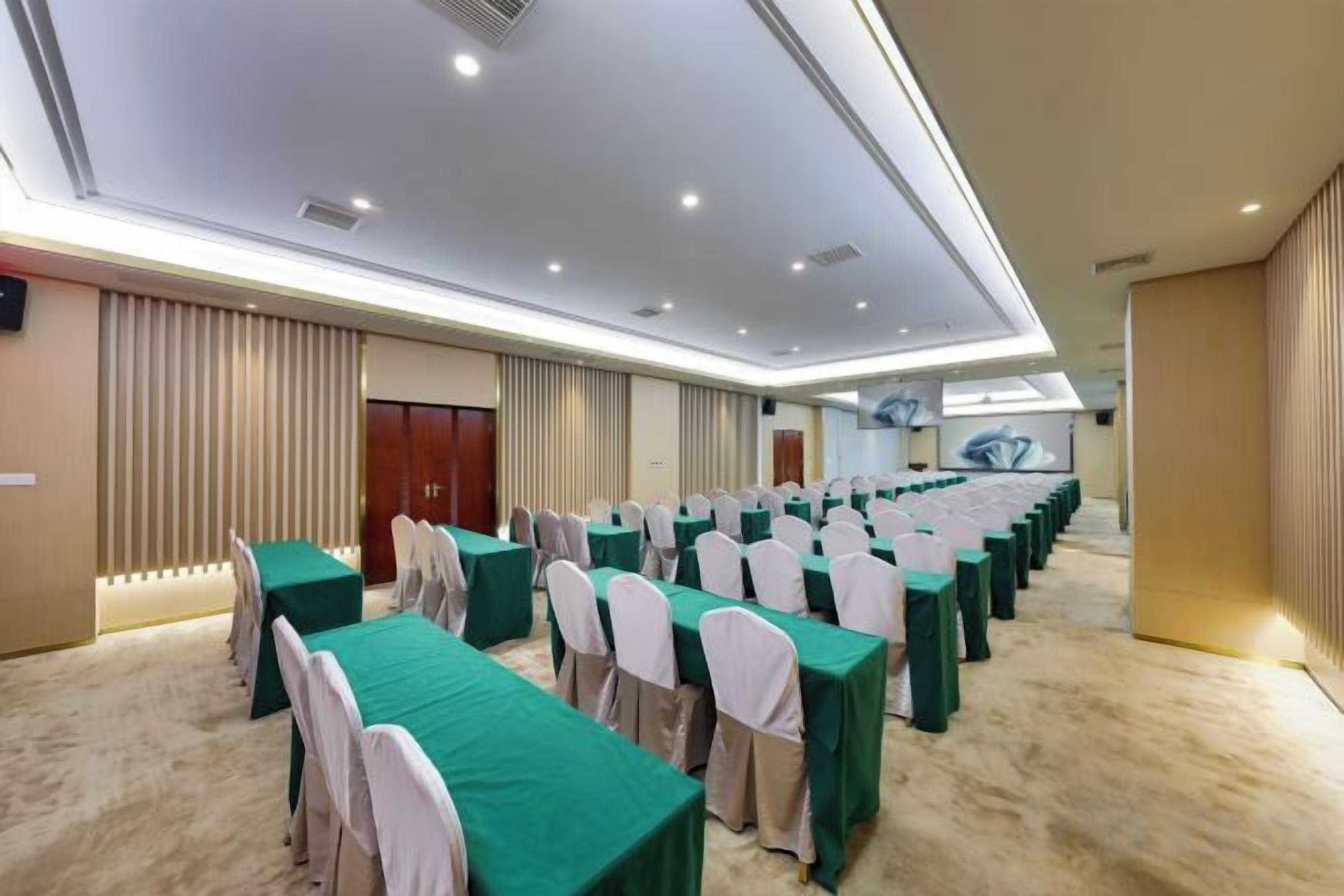 A conference room with rows of tables and chairs, a carpeted floor, and a high ceiling with recessed lighting.