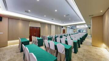 A conference room with rows of tables and chairs, a carpeted floor, and a high ceiling with recessed lighting.