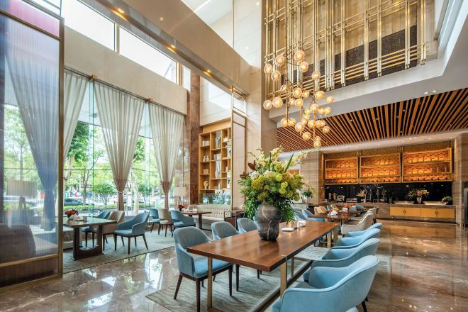 A spacious hotel lobby with a high ceiling, a bar area, and seating arrangements.