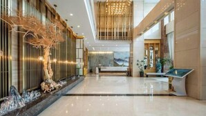 A spacious lobby with a reception desk, a large chandelier, and a modern art piece.