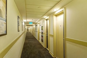 Un pasillo de hotel con puertas a ambos lados, cuadros en las paredes y suelo alfombrado.