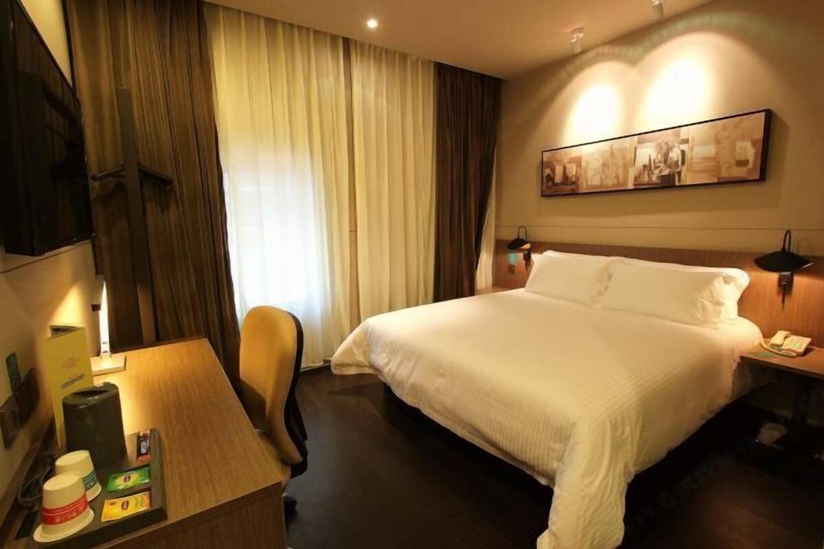 Une chambre d’hôtel comprenant un lit, un bureau avec une lampe, une chaise, une table de chevet avec un téléphone et une œuvre d’art accrochée au mur.