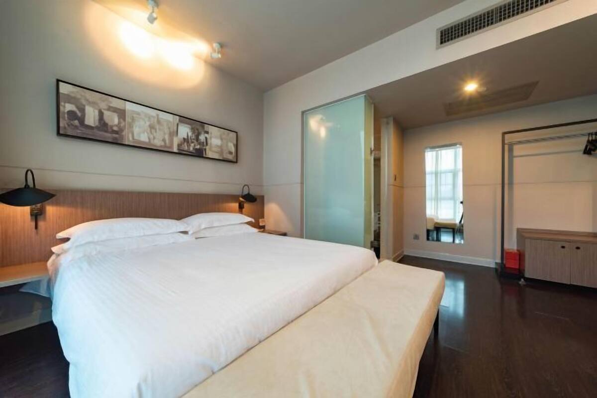 Une chambre d’hôtel avec un grand lit, une œuvre d’art accrochée au mur, une lampe de chevet et une porte coulissante donnant accès à la salle de bain.