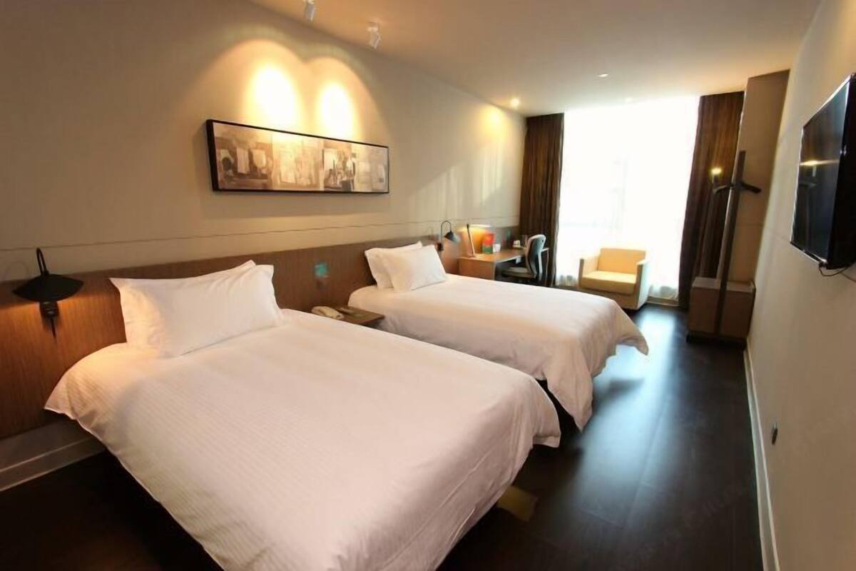 Une chambre d’hôtel avec deux lits, un bureau, une chaise, une télévision et un tableau au mur.