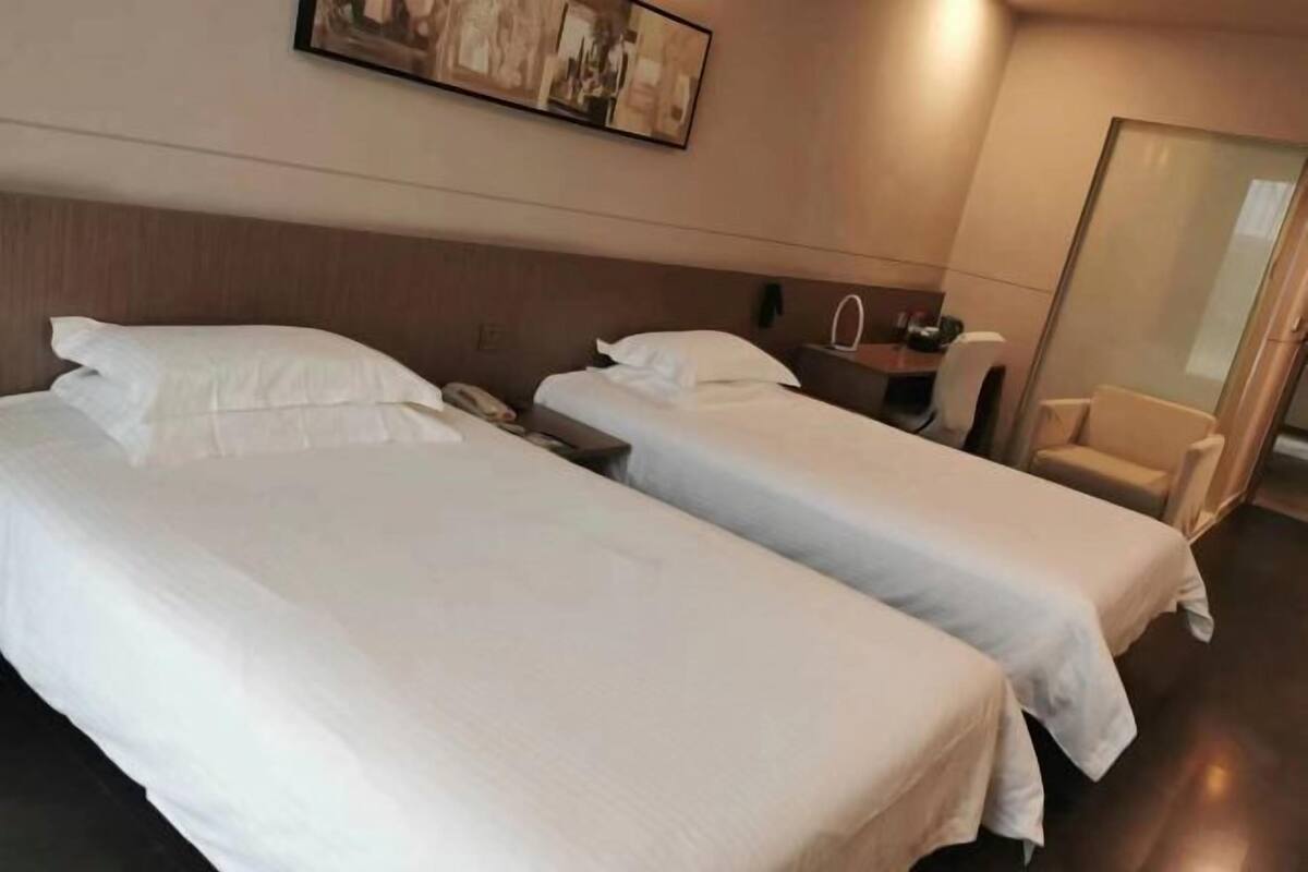 Une chambre d’hôtel avec deux lits, un bureau, une chaise et une cloison en verre.