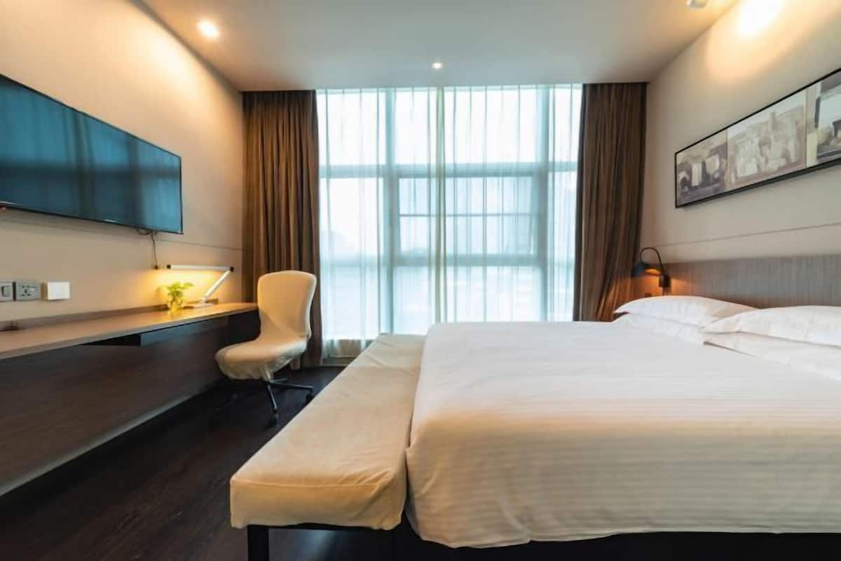 Une chambre d’hôtel avec un lit, un bureau, une chaise, une télévision et une fenêtre avec des rideaux.
