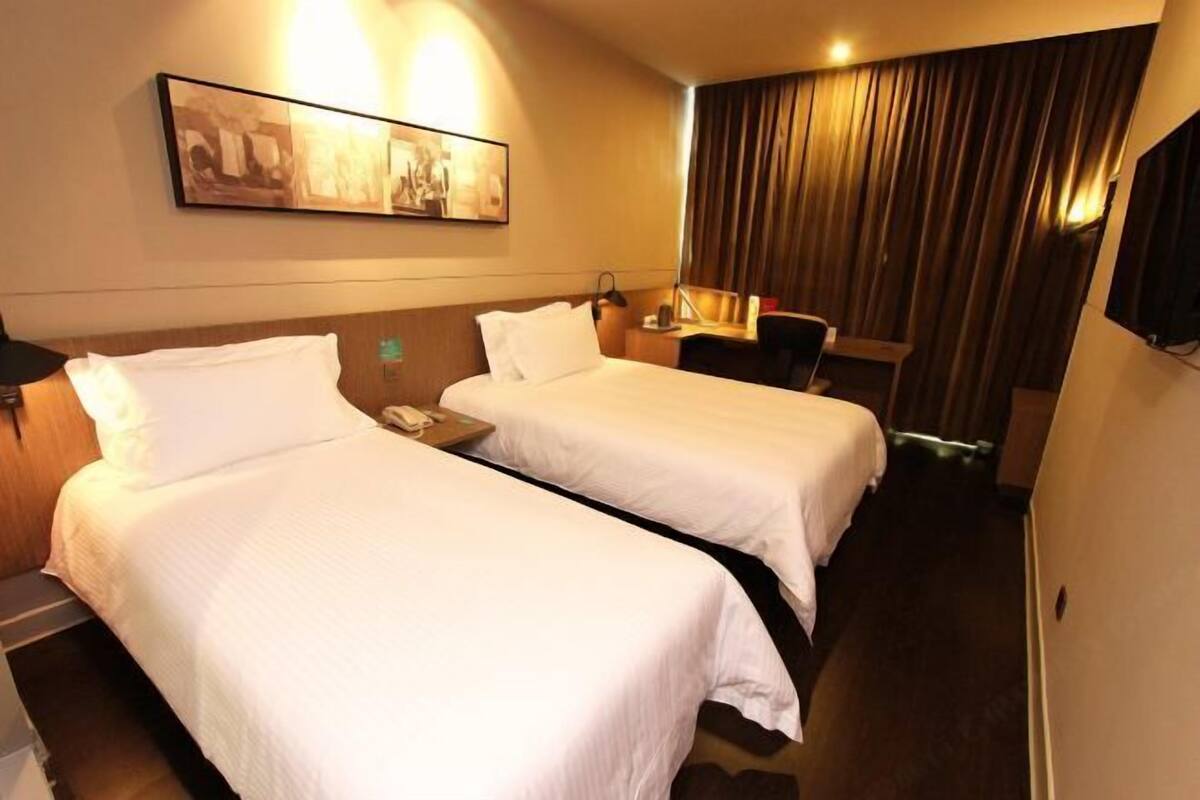 Une chambre d’hôtel avec deux lits simples, un bureau avec une chaise, un téléphone et un téléviseur fixé au mur.
