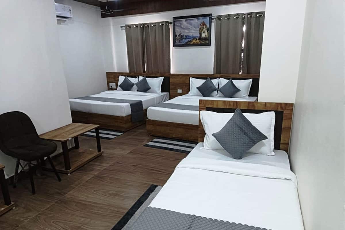 A hotel room with two single beds, a sofa bed, a wooden table, and a chair.