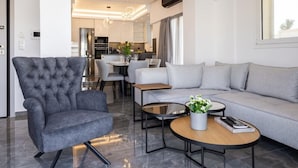 A modern living room with a grey armchair, a grey sofa, and a coffee table with a vase of flowers. - Parthenon View Luxury Penthouse (Athens)